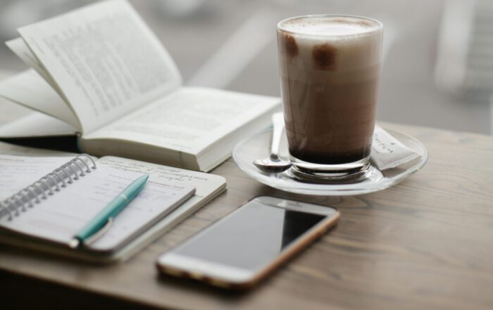 Morgenroutine: Kaffee, Buch, Notizbuch und Smartphone liegen auf einem Tisch.